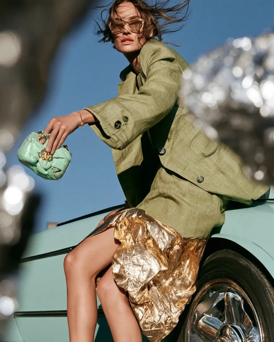 Woman in a green suit and gold skirt seated on a mint car