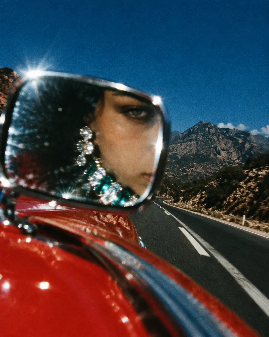 Face reflected in a car wing mirror wearing emerald earrings