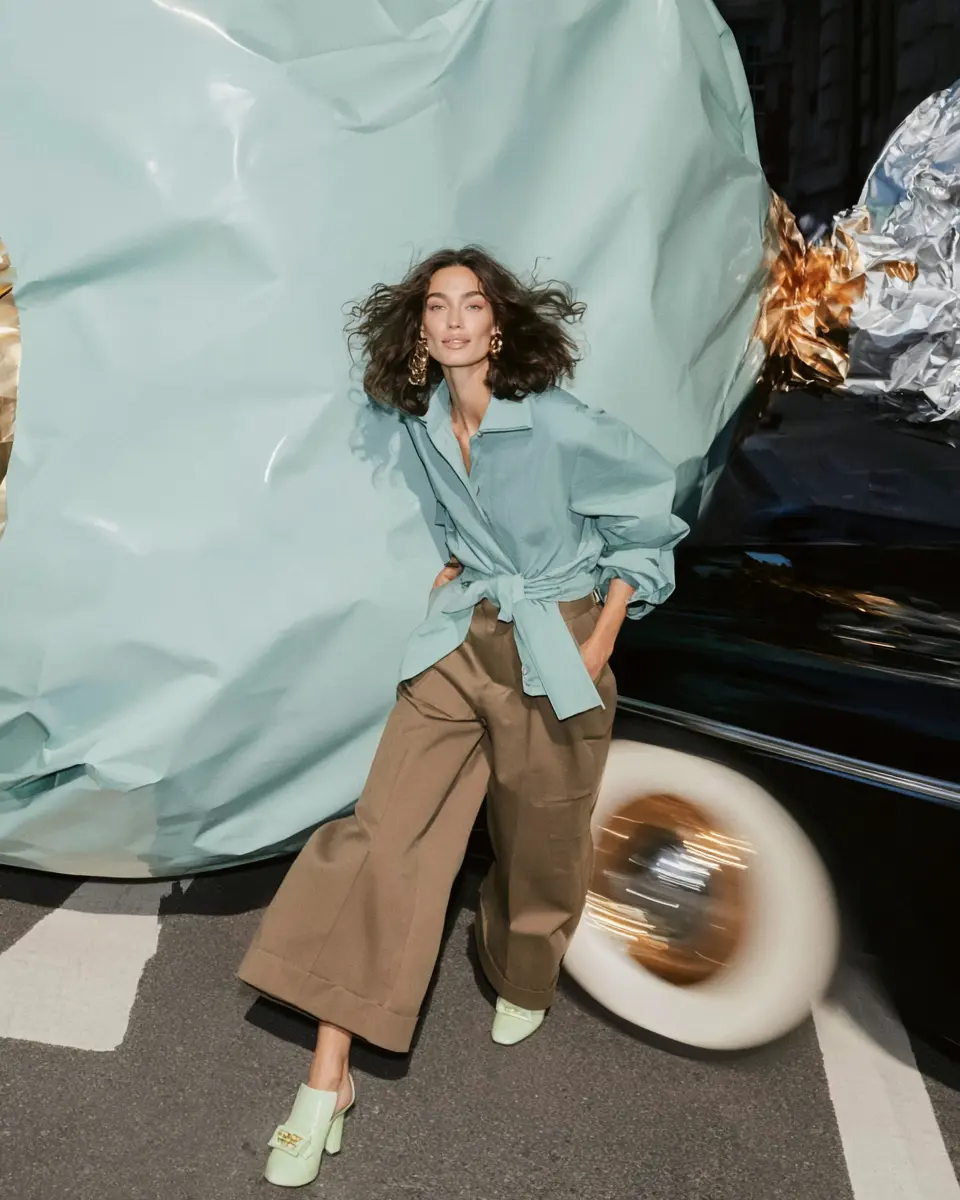 Woman in a pale blue shirt before a giant wrapped form and a moving car