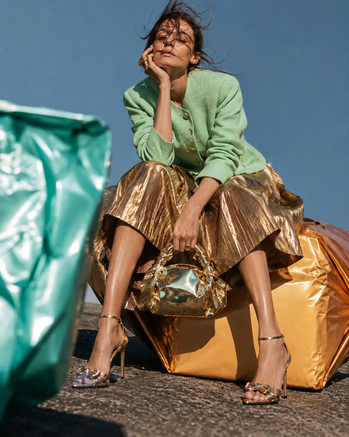 Woman in a mint jacket and gold skirt seated on a giant gold-wrapped form