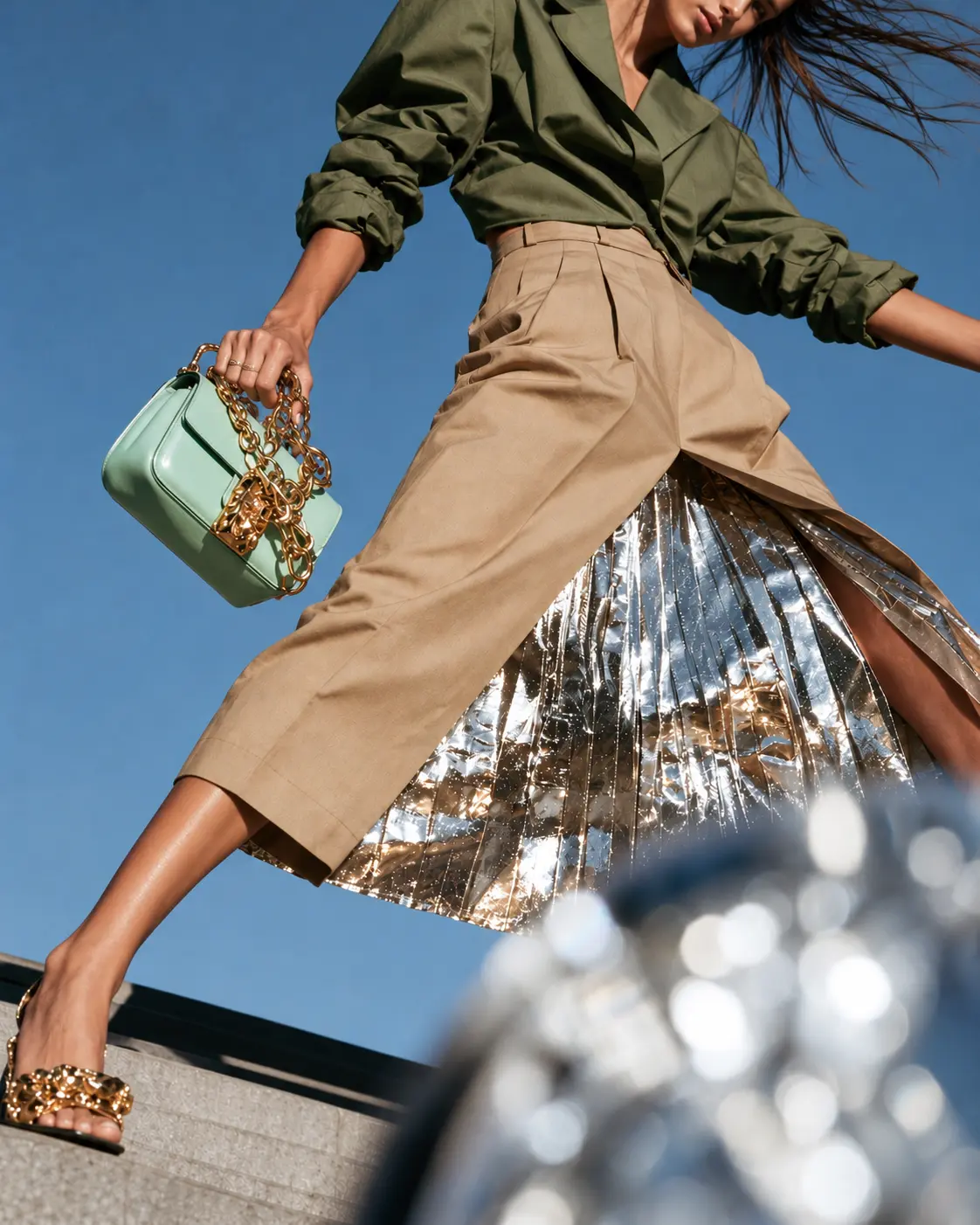 Low angle of a woman with a mint chain bag and silver pleated skirt