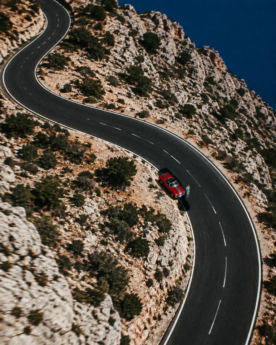 Aerial view of a winding mountain road with a red convertible